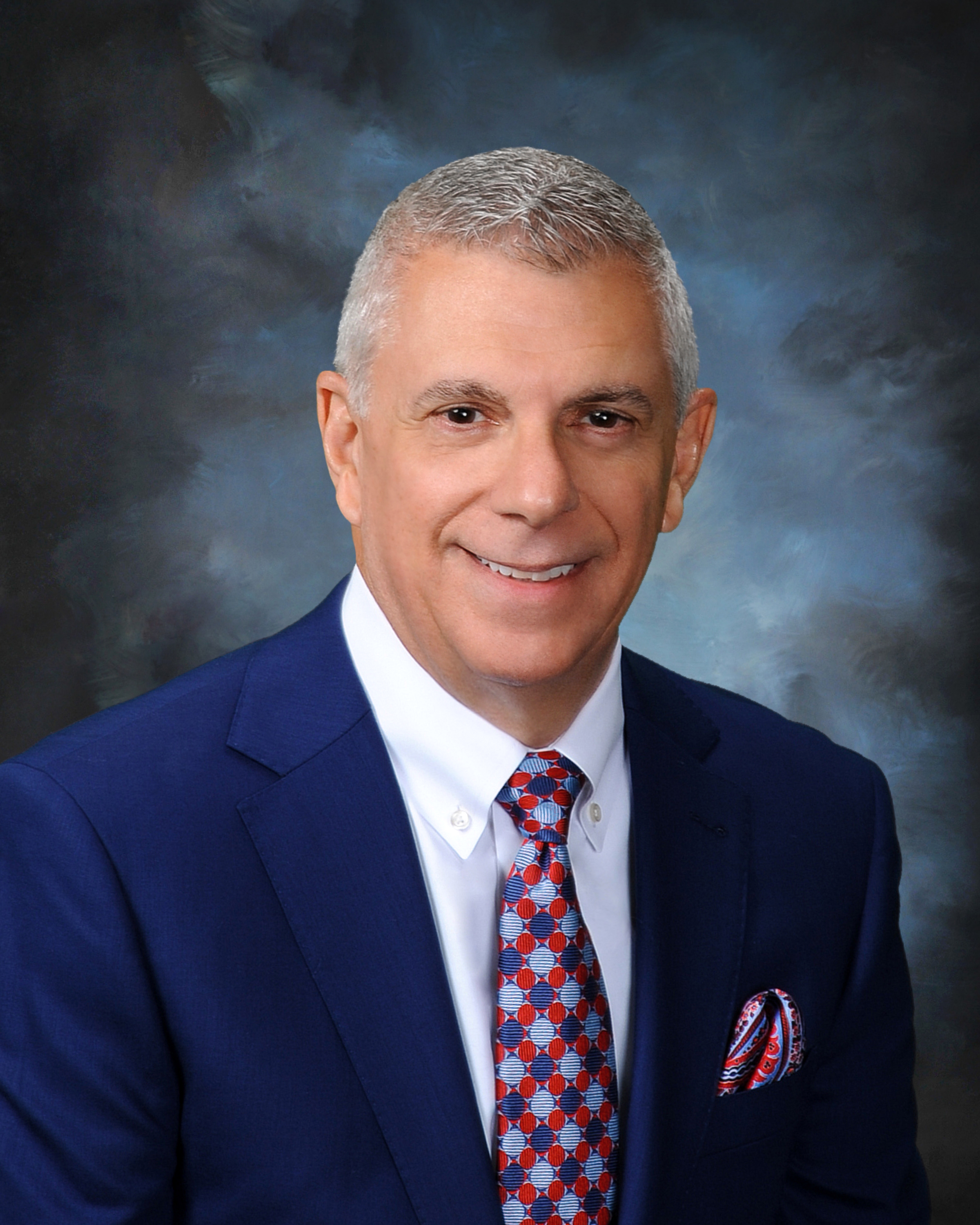 Anthony Picente in blue suit, white shirt and burgundy patterned tie, smiles.