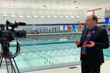 Professor Paul MacArthur stands next to the UC Pool discussing the Olympics.