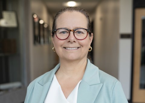 Sharon Kanfoush in a green blazer and red glasses, smiles at the camera.