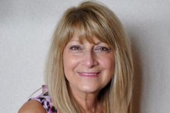 Rosemary Bonacci stands in front of a white wall and smiles.