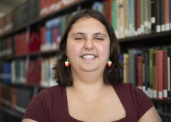 Dominica Witt in burgundy shirt stands in front of the library stacks.