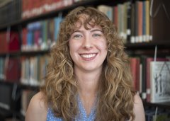 Elise Thompson in blue shirt stands in front of library stacks.
