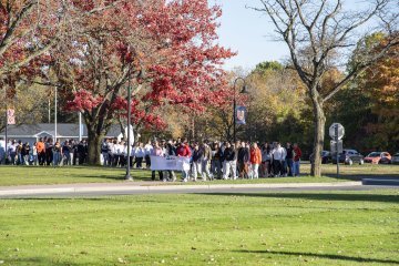 A crowd of people circle around Bull Hall carrying a banner promoting unity.