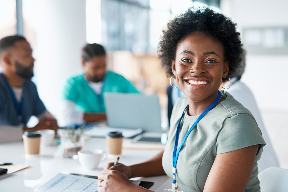 An African American healthcare administrator smiles at the camera while working at a table with other healthcare professionals.
